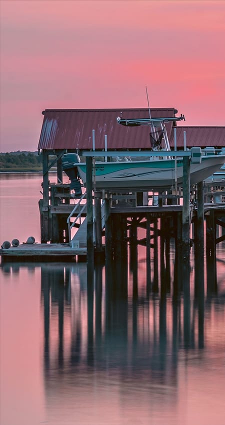 A covered boat lift on a dock at sunset, reflected in still water.