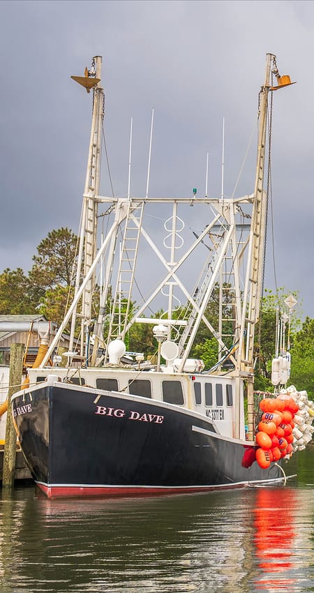 A trawler named Big Dave moored at a dock, outriggers raised, with orange buoys hanging from its side.