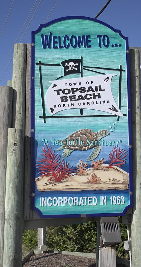 The Welcome to Topsail Beach town sign, painted with a sea turtle, on tall wooden posts.